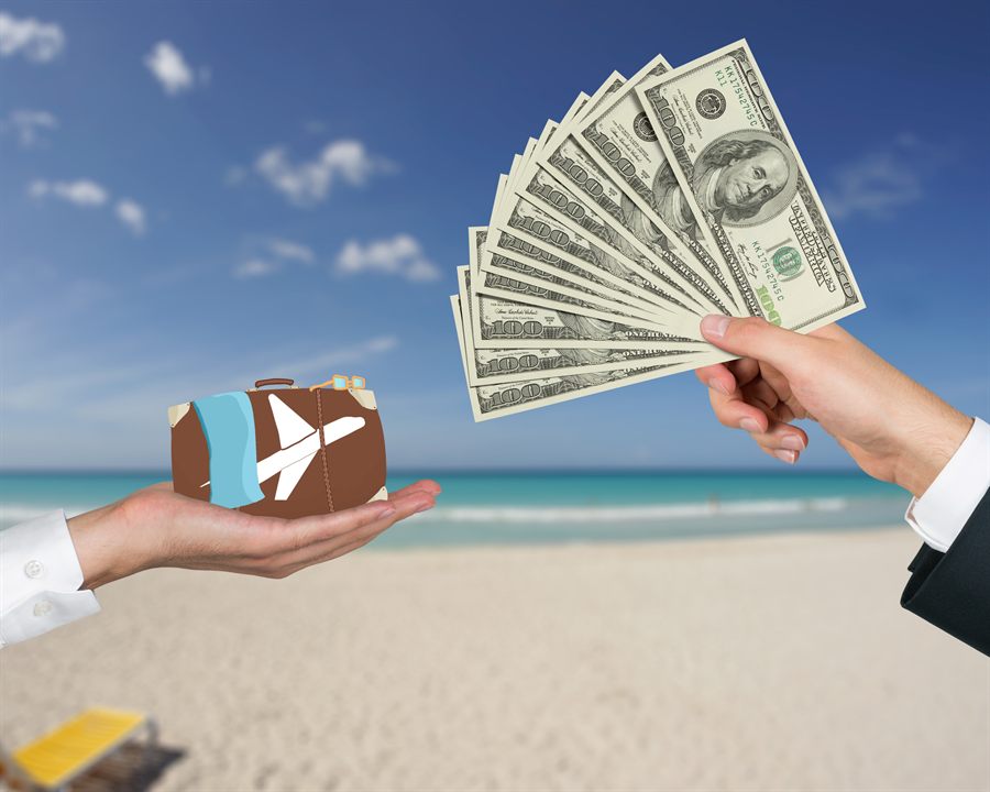Hand holding out banknotes to a hand holding a small suitcase on a beach