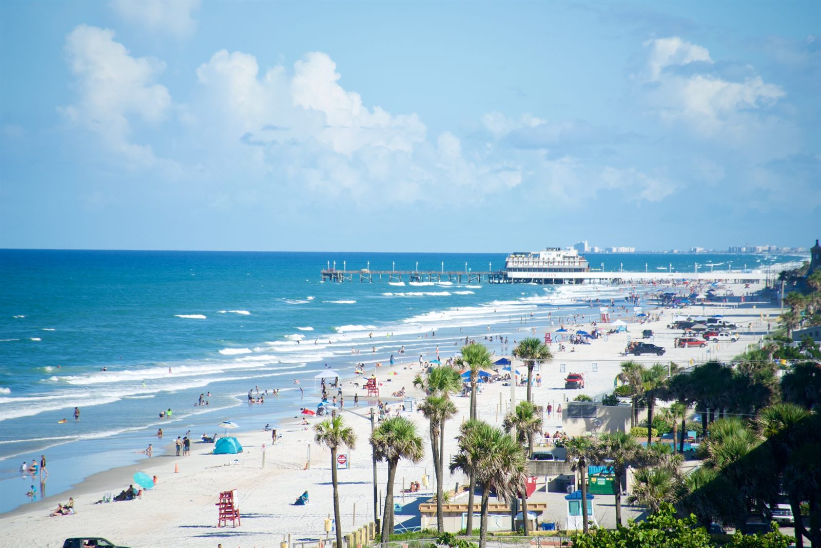 Busy Florida beach and ocean with a pier in the distance